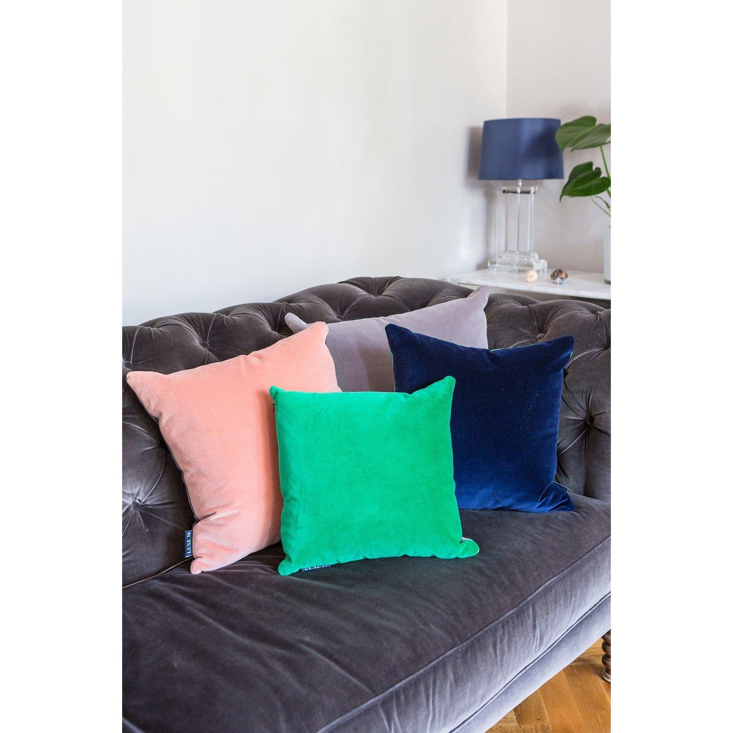 Blush pink velvet cushion and navy velvet cushion and emerald green velvet cushion on a velvet sofa