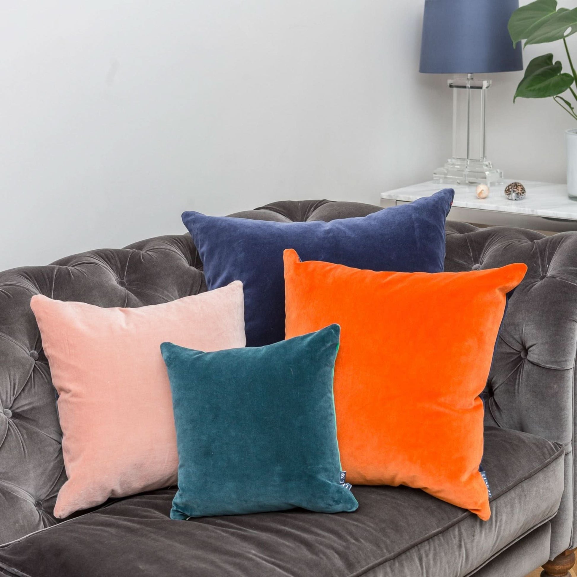 bright orange and navy reversible velvet cushions with blush pink and teal cushions on a velvet sofa