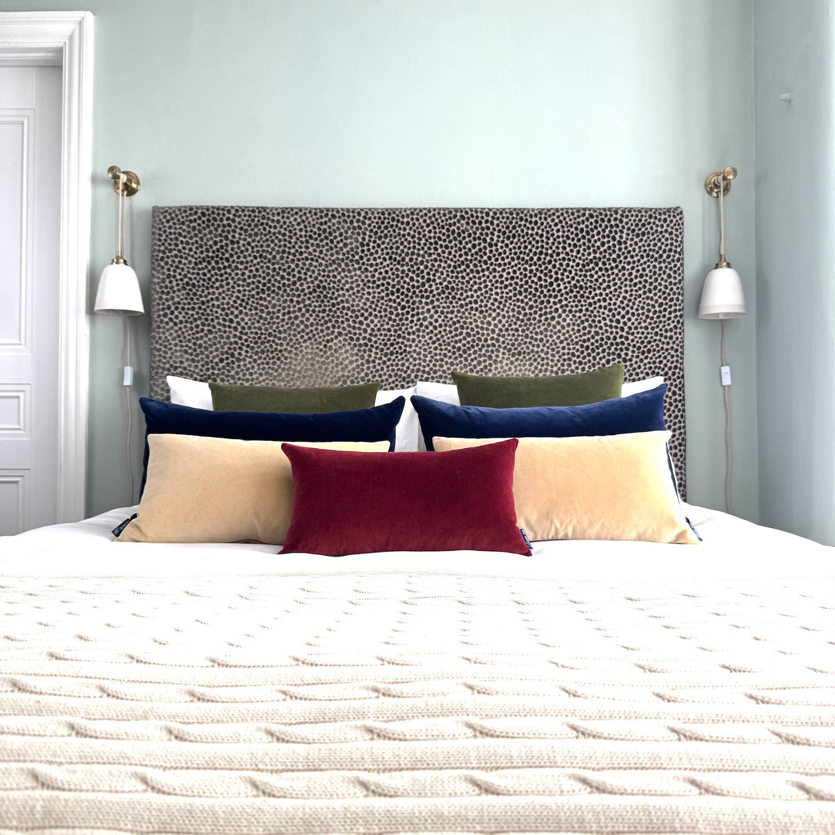 burgundy velvet rectangle cushion styled on a bed in a blue room