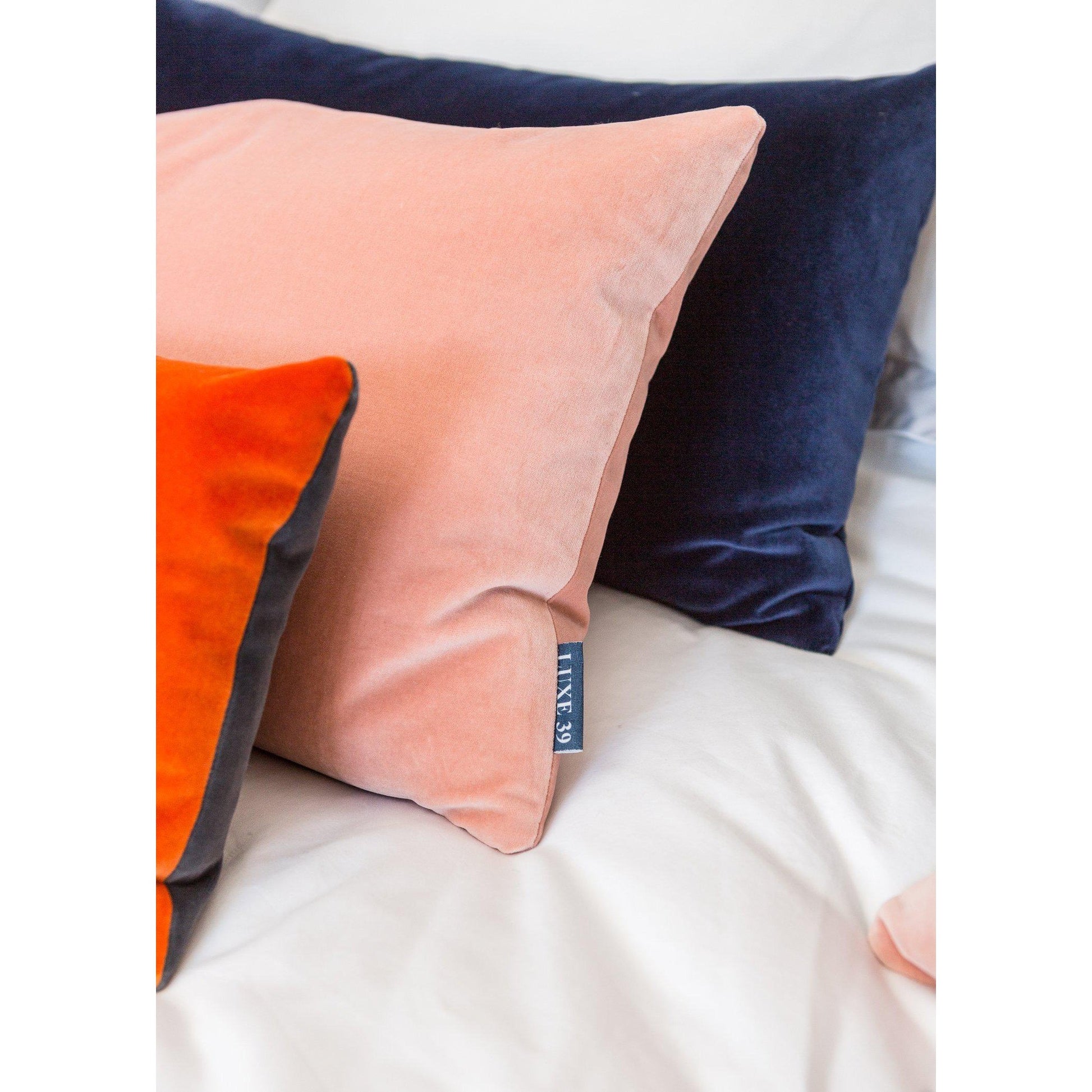 navy and burnt orange cushions with blush pink on a bed