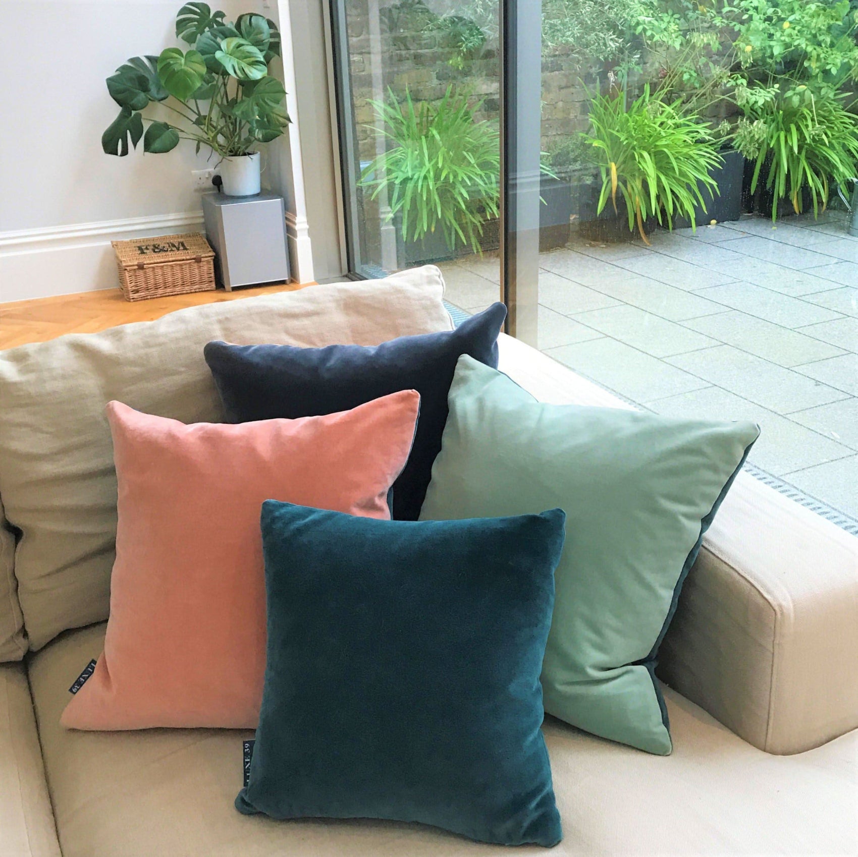 teal pink cushion with duck egg and dark grey velvet cushions on a cream linen sofa
